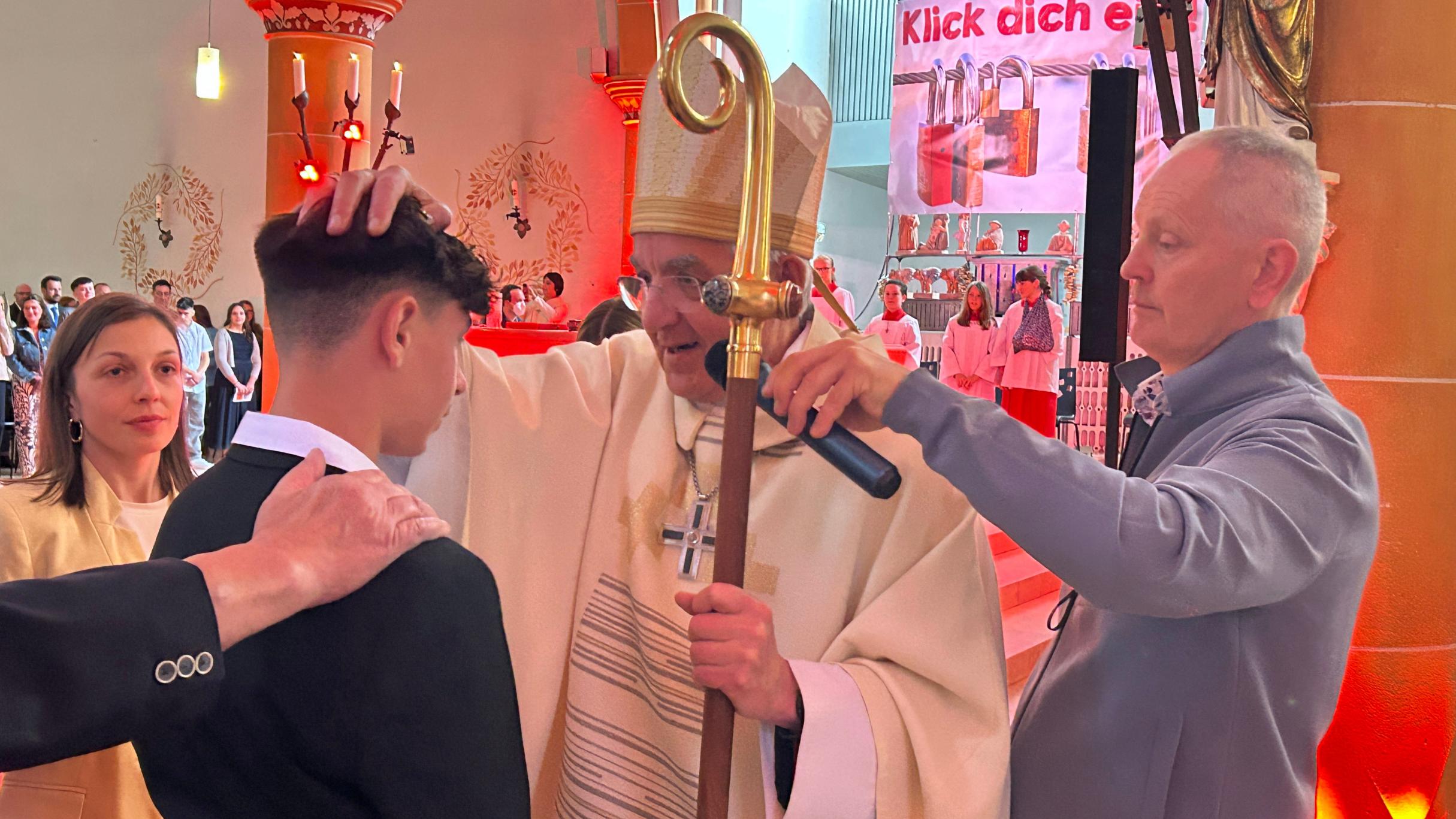 Ein Weihbischof mit Bischofsstab legt einem jungen Mann die Hand zur Firmung auf